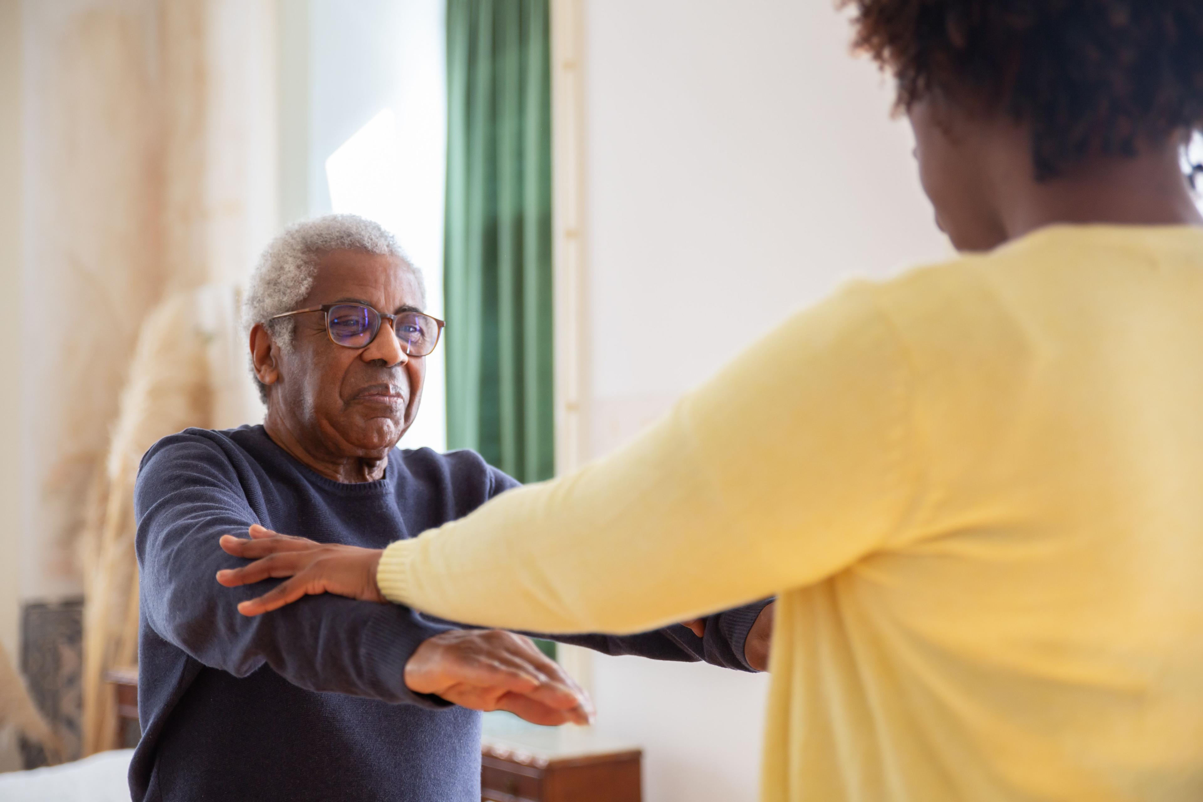 Physiotherapist guiding an older man through an arm exercise during a home visit falls prevention session